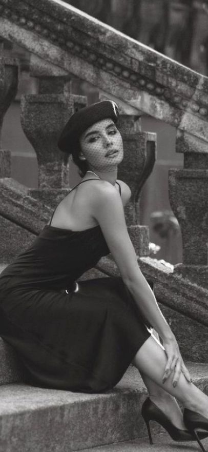 Woman in a black dress and beret with a veil, sitting on stone steps