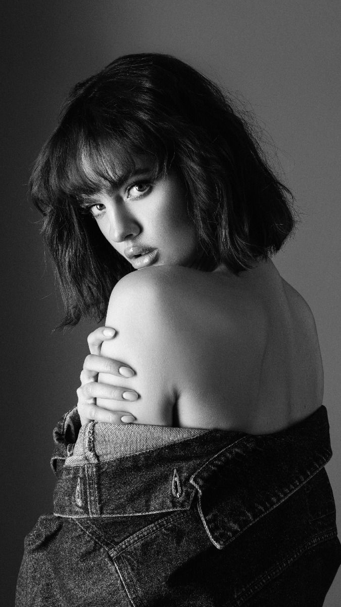 Woman with short hair and a denim jacket draped over her shoulders, looking over her shoulder