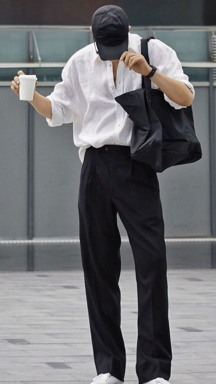 Person in a white shirt and black pants holding a coffee cup and tote bag