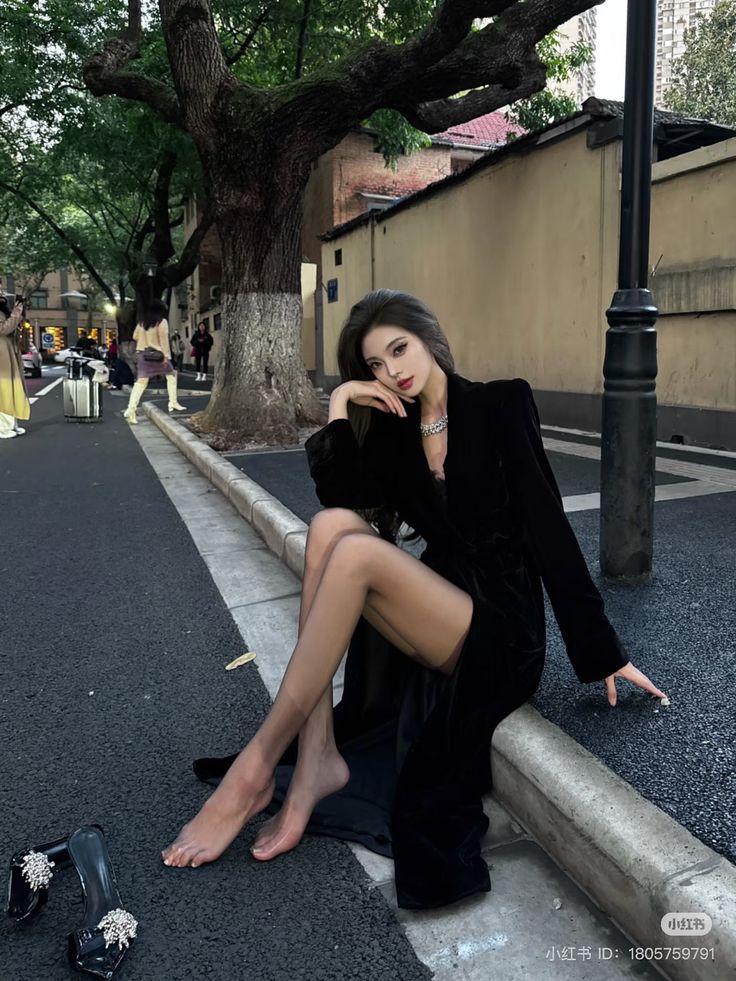 Woman in a black dress and sheer stockings sitting on a street curb at night