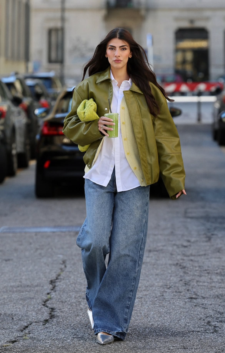 Woman with long dark hair wearing a green jacket and wide leg jeans on a street