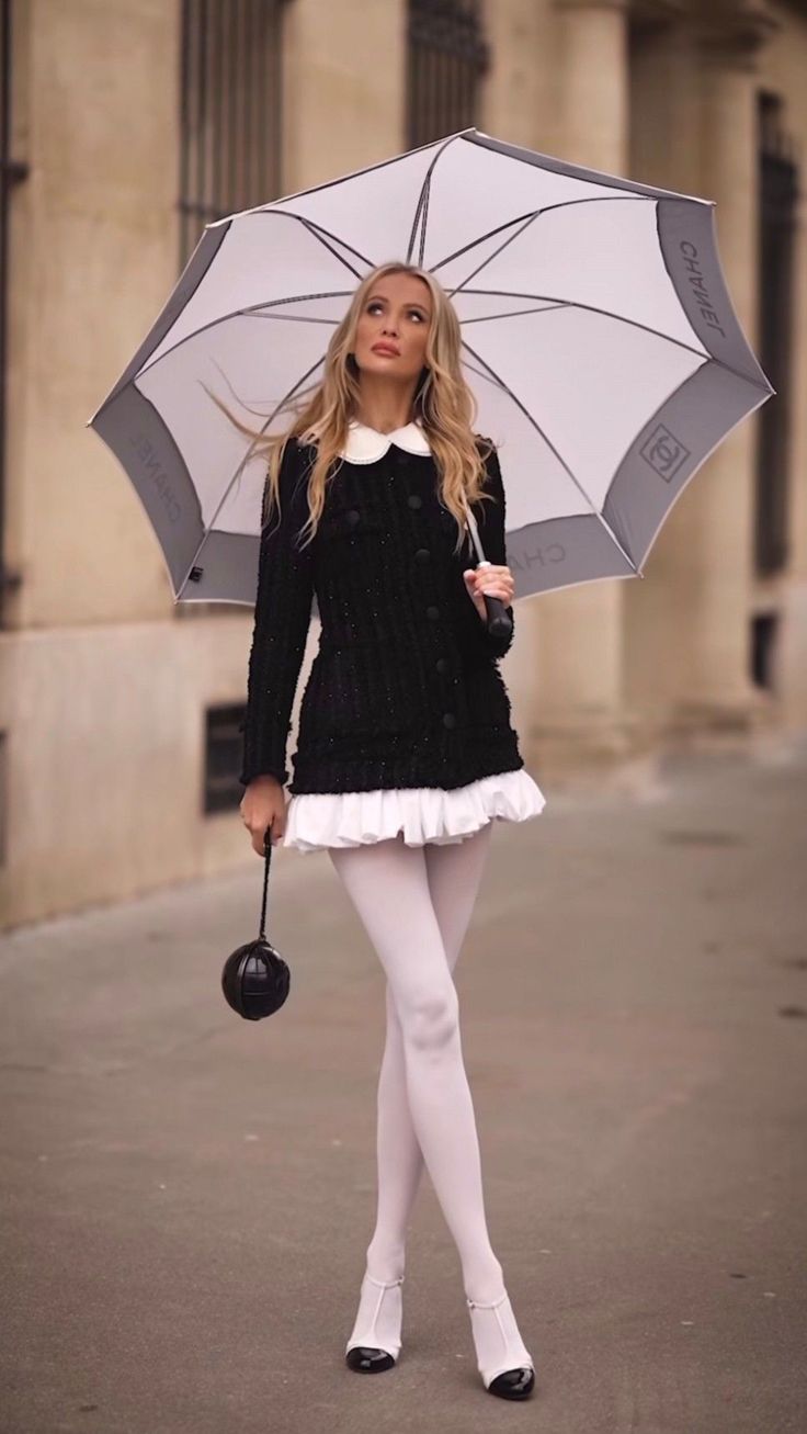 Woman in a black jacket with a white collar and white tights holding an umbrella