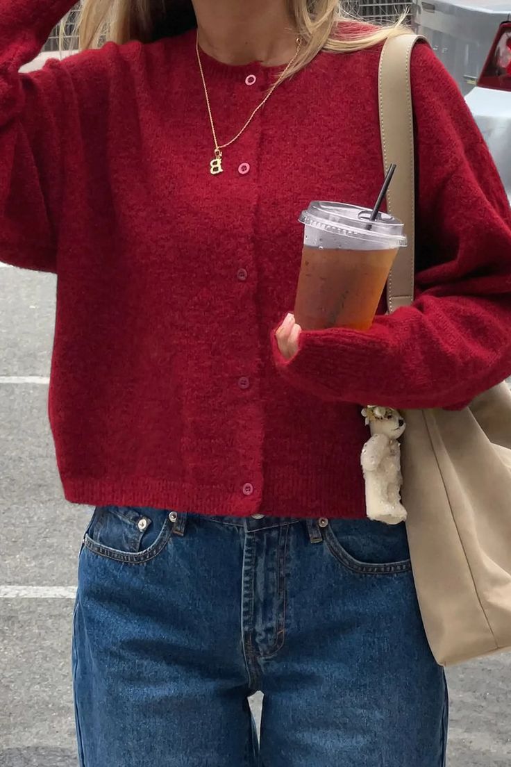 Person in a red cardigan and blue jeans holding an iced tea