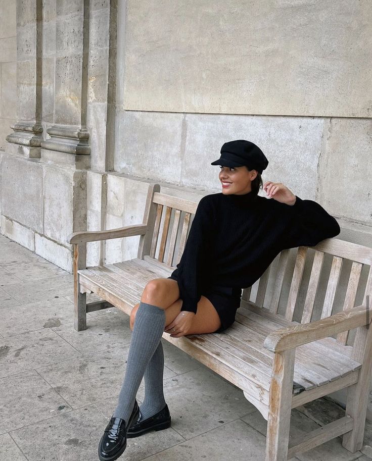 Woman in a black sweater and shorts with knee-high socks sitting on a bench