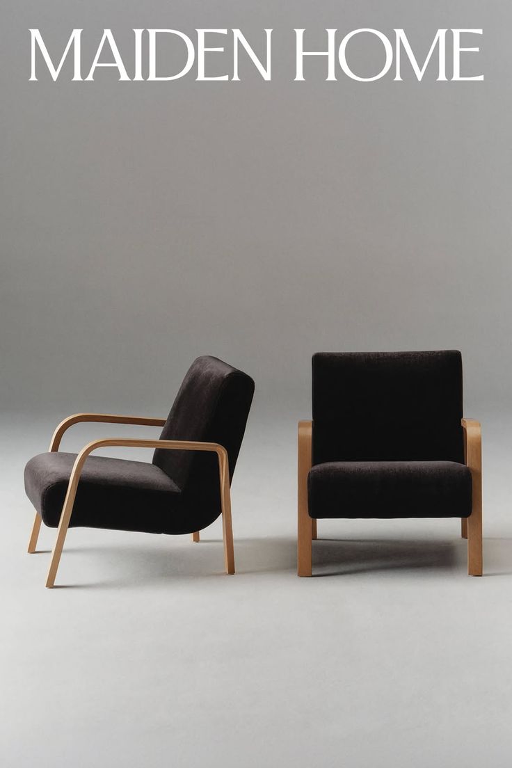 Two armchairs with wooden frames and dark upholstery in a studio setting