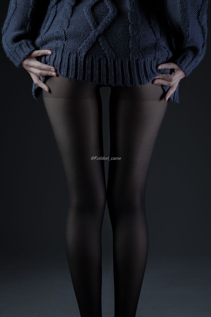 Person wearing a dark knitted sweater and black tights against a dark background