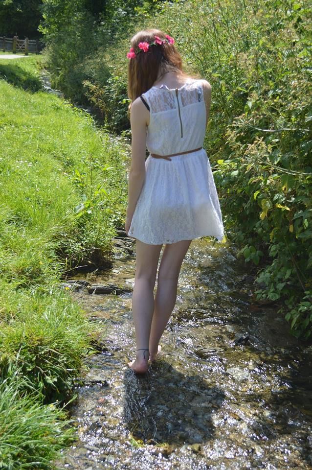 Woman in a white dress and flower crown walking barefoot in a stream