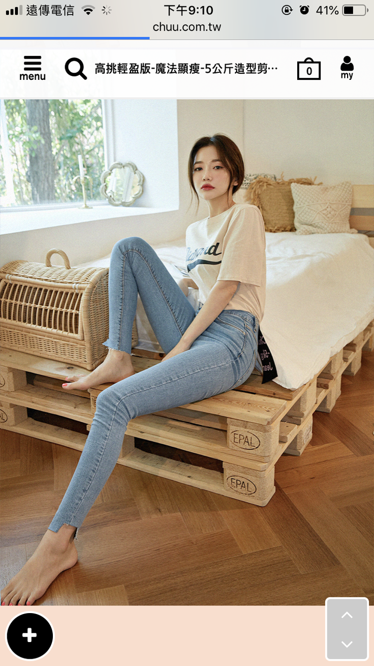 Woman in a t-shirt and skinny jeans sitting on a pallet bed indoors