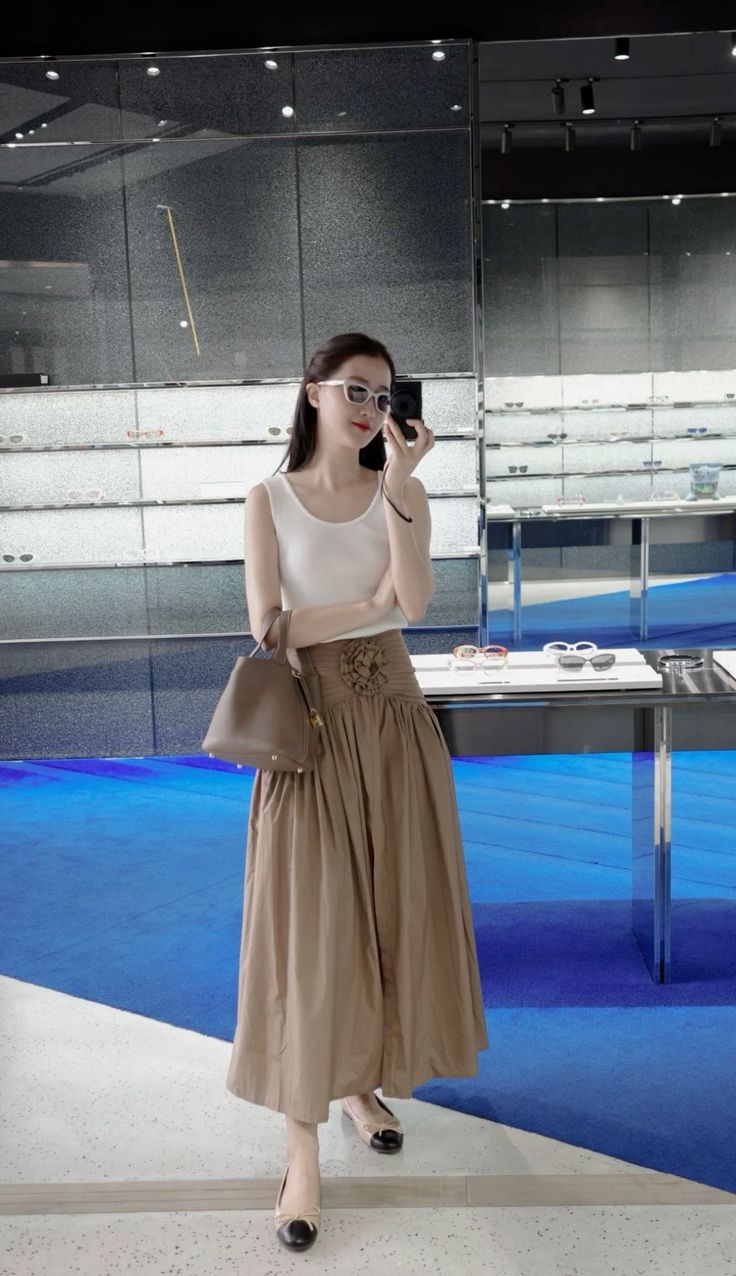 Woman in a white tank top and midi skirt taking a mirror selfie in a store