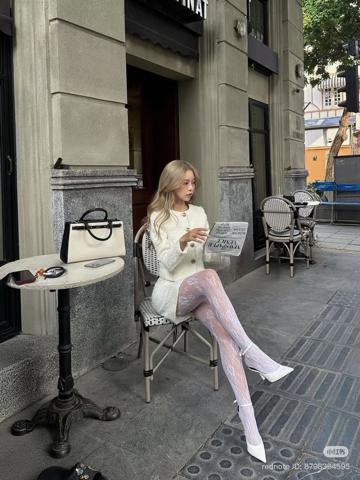 Woman with blonde hair in a white outfit and lace tights sitting at an outdoor cafe