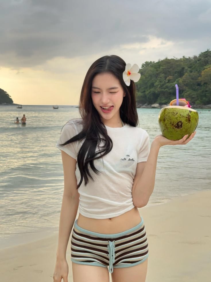 Woman with long hair holding a coconut drink on a beach