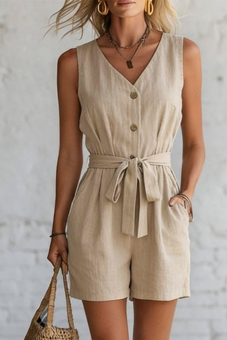 Woman in a beige sleeveless jumpsuit with a belted waist and layered necklaces