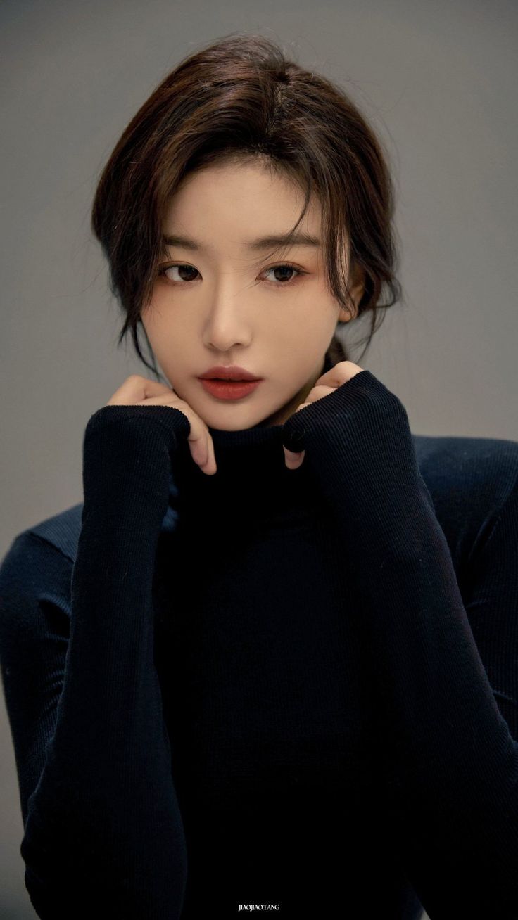Woman in a dark turtleneck with hands near her chin, looking away