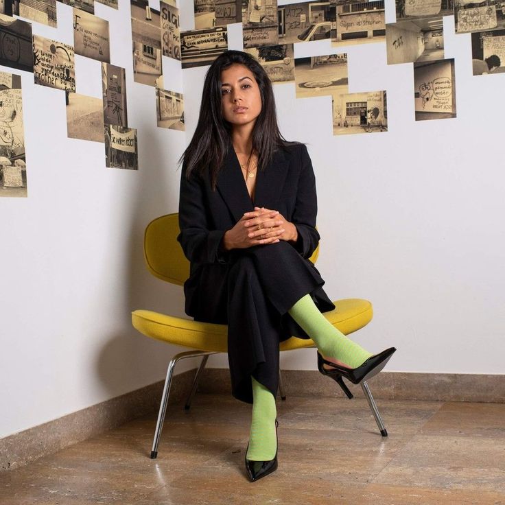 Woman in a black suit and lime green socks sitting on a yellow chair indoors