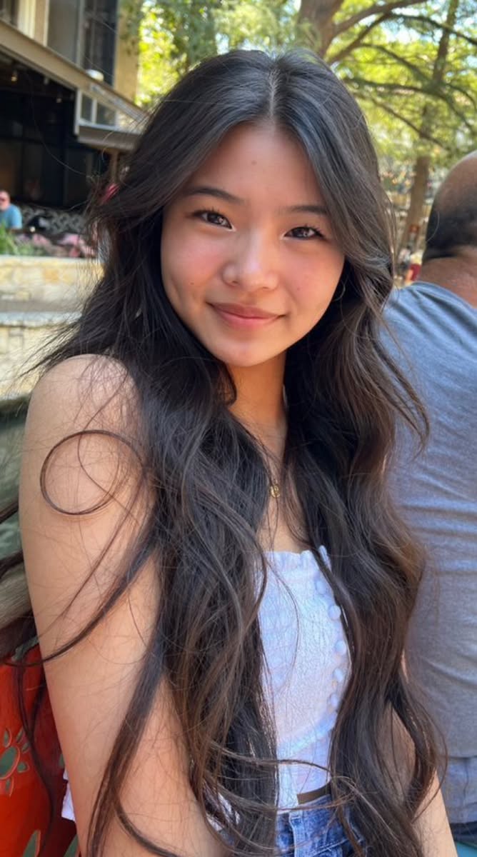 Young woman with long brown hair smiling outdoors in daylight