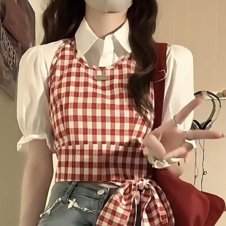 Person in a red gingham crop top and white shirt making a peace sign