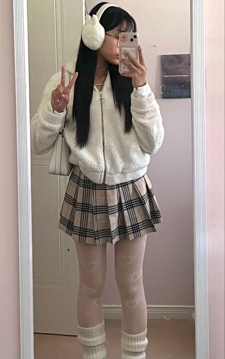 Person in a white jacket and plaid skirt taking a mirror selfie