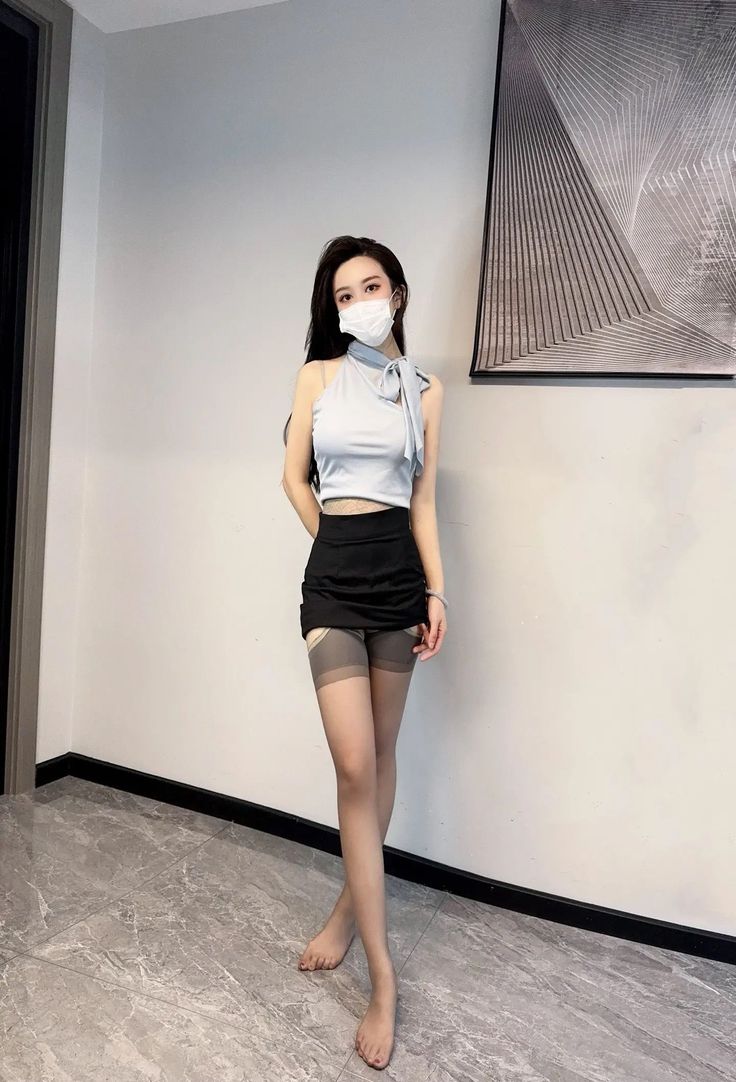 Woman in a halter top, mini skirt, and sheer tights posing indoors
