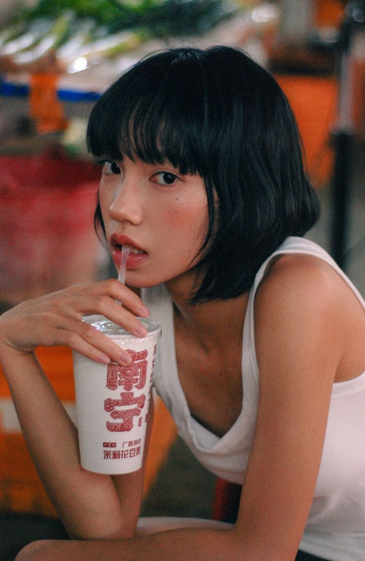 Woman with short black hair drinking from a cup with a straw