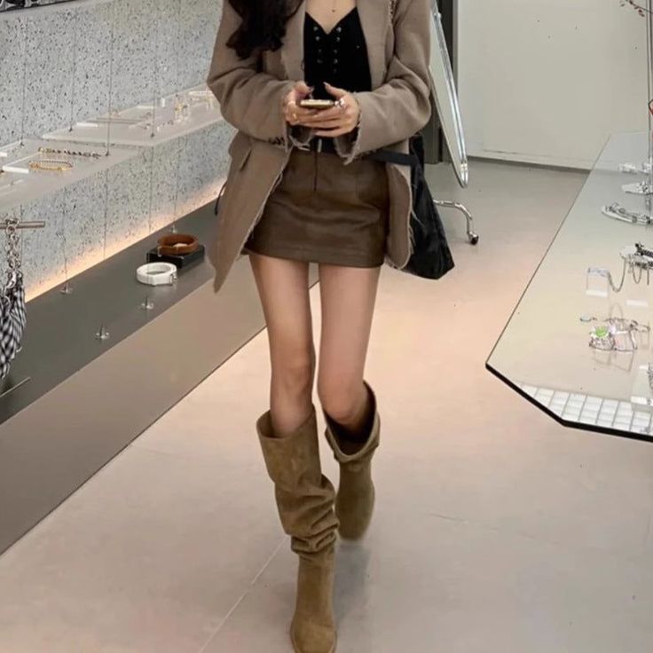 Person in a brown blazer and mini skirt with knee-high boots indoors
