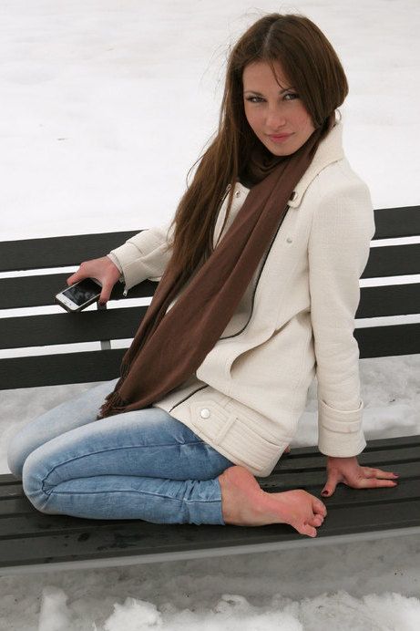 Woman with long hair sitting on a bench in the snow, holding a phone