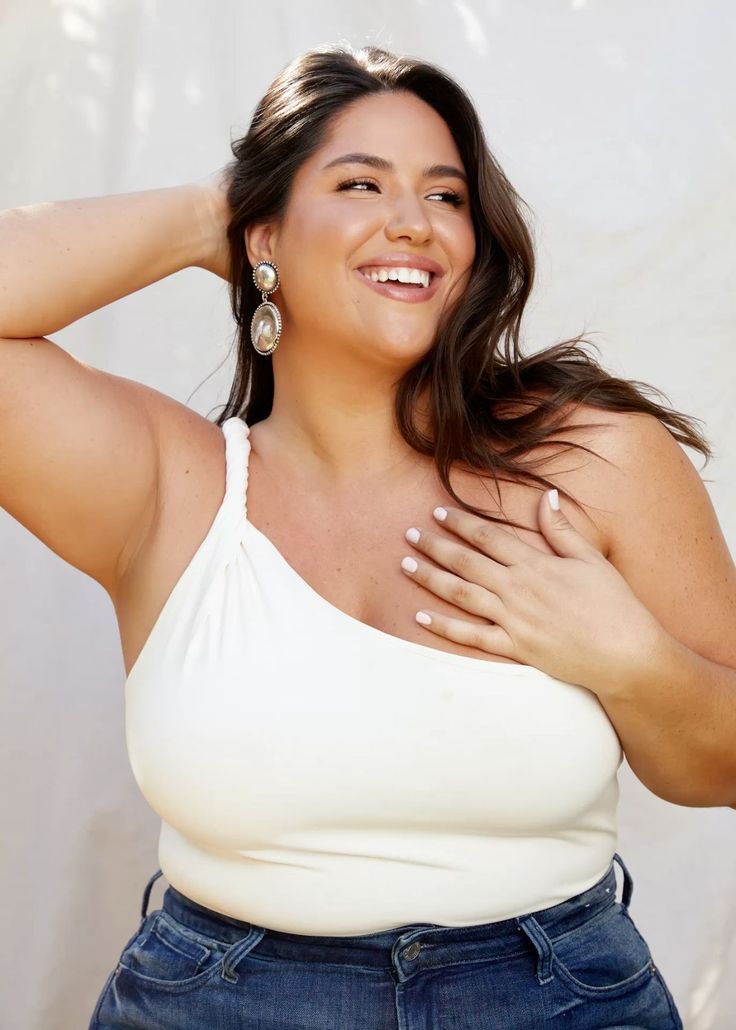 Woman with long dark hair wearing a white top and jeans, smiling