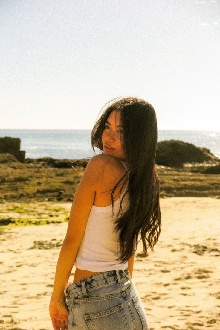 Woman with long dark hair on a beach at golden hour, looking over her shoulder