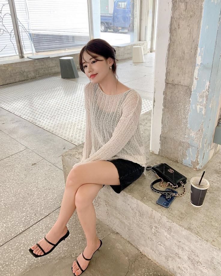 Woman in a sheer top and black shorts sitting indoors
