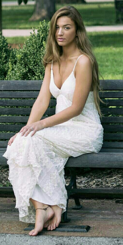 Woman in a white dress sitting barefoot on a park bench