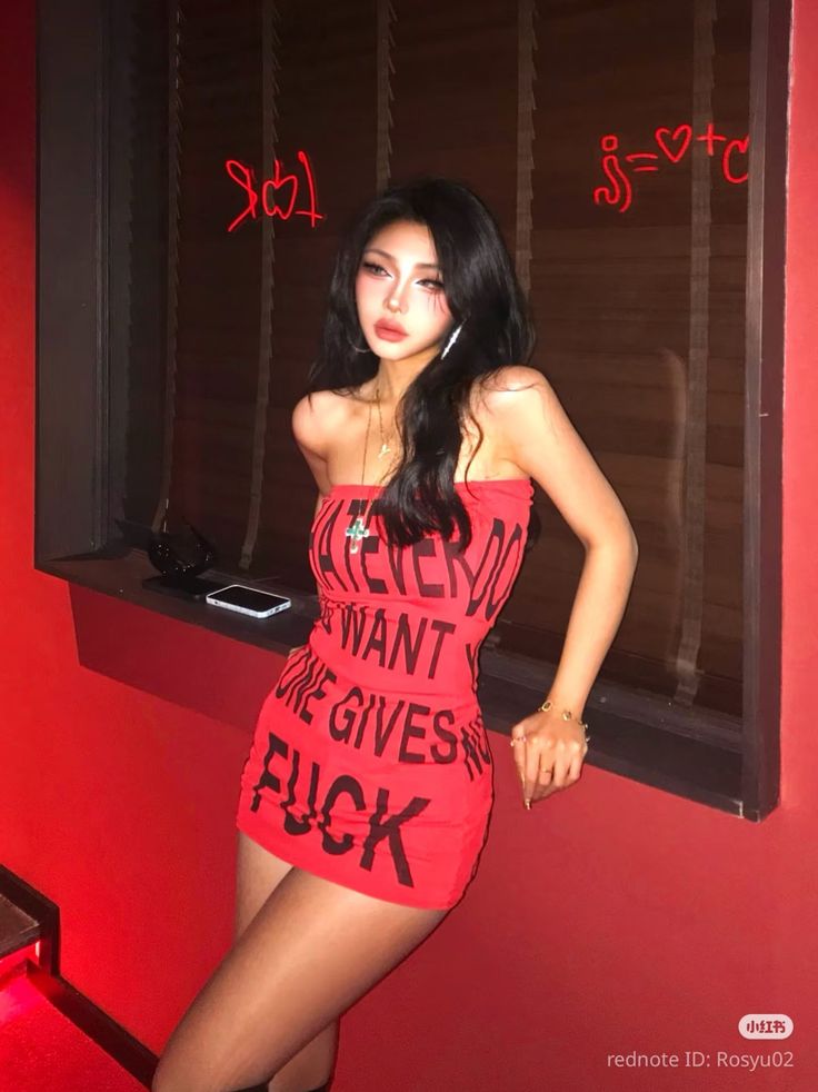 Woman in a red strapless dress with text, leaning against a wall