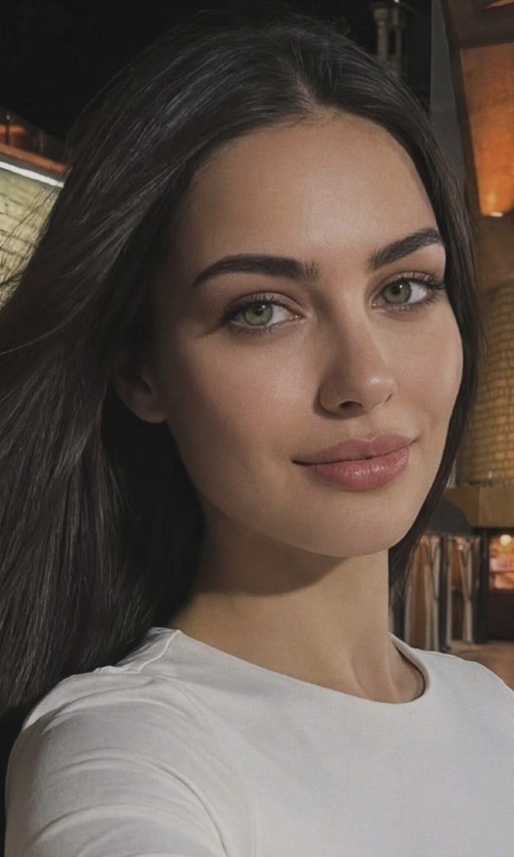 Woman with long dark hair and green eyes wearing a white shirt indoors