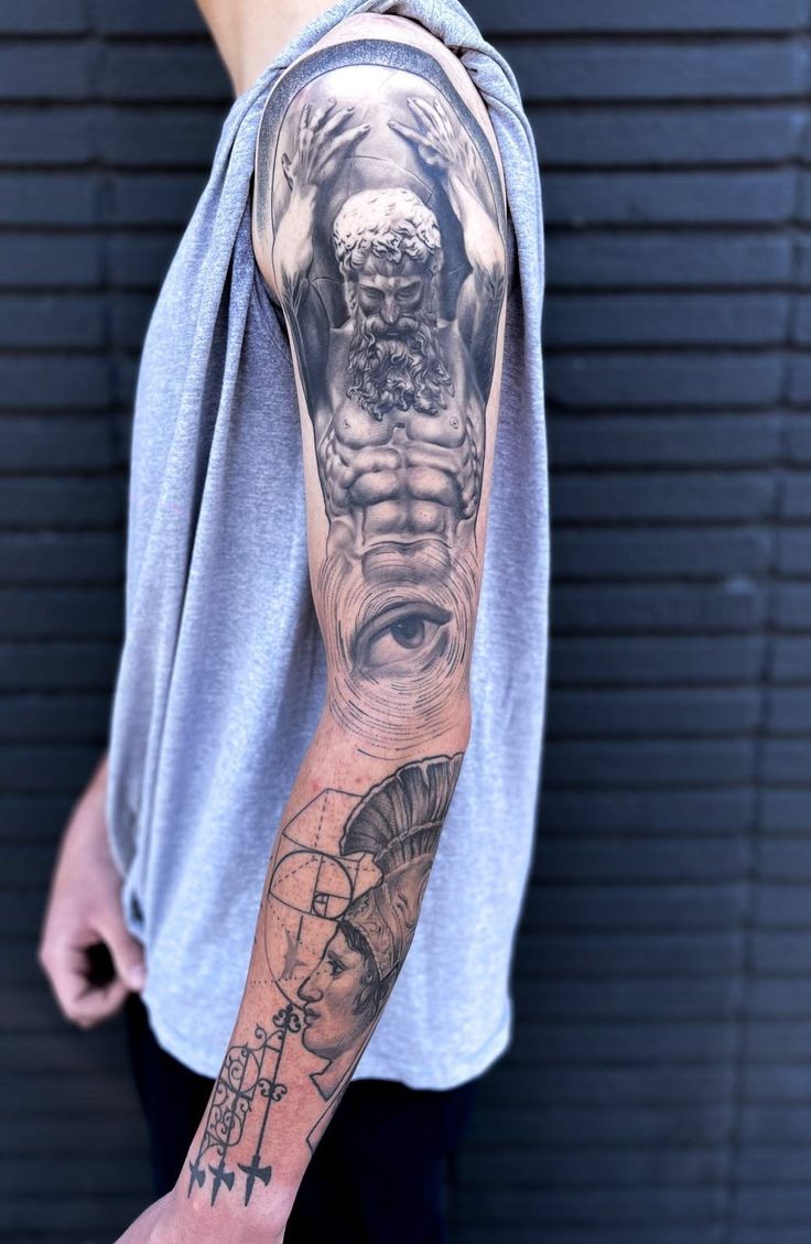 Arm with a detailed black and grey tattoo featuring a mythological figure and an eye