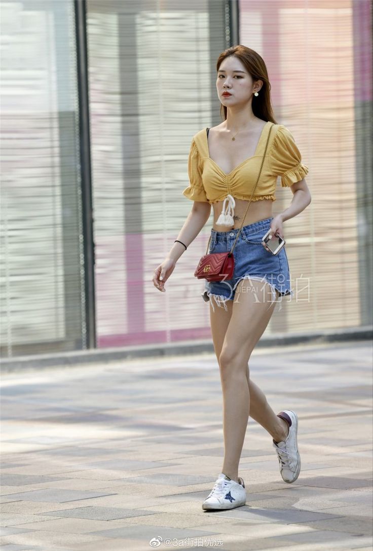Woman in a yellow crop top and denim shorts walking on a street