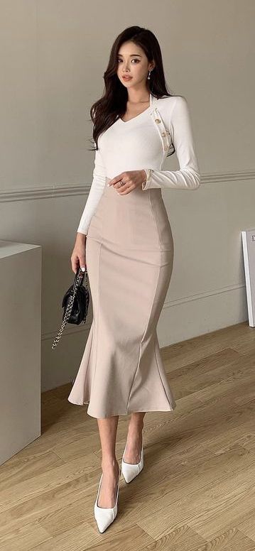 Woman in a white top and mermaid skirt holding a black handbag indoors