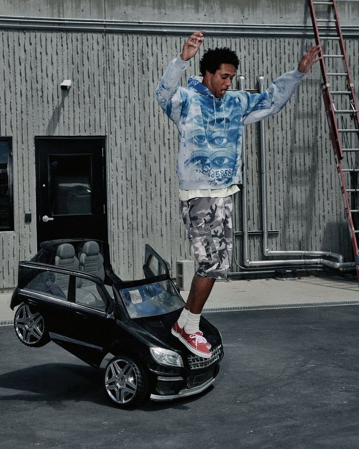 Man in a blue hoodie and camo shorts balancing on a toy car