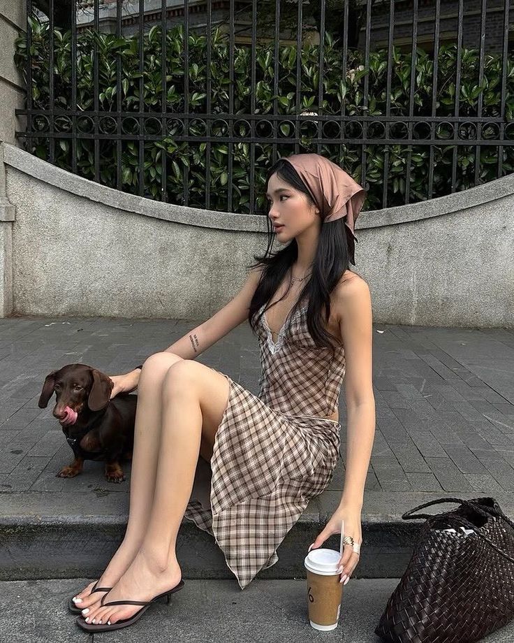 Woman in a plaid dress and bandana sitting outdoors with a dachshund
