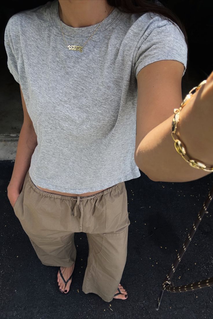 Person in a gray t-shirt and khaki pants with a gold necklace and bracelet