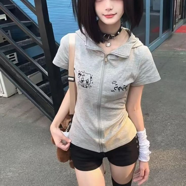Person with short black hair wearing a grey hoodie and black shorts outdoors