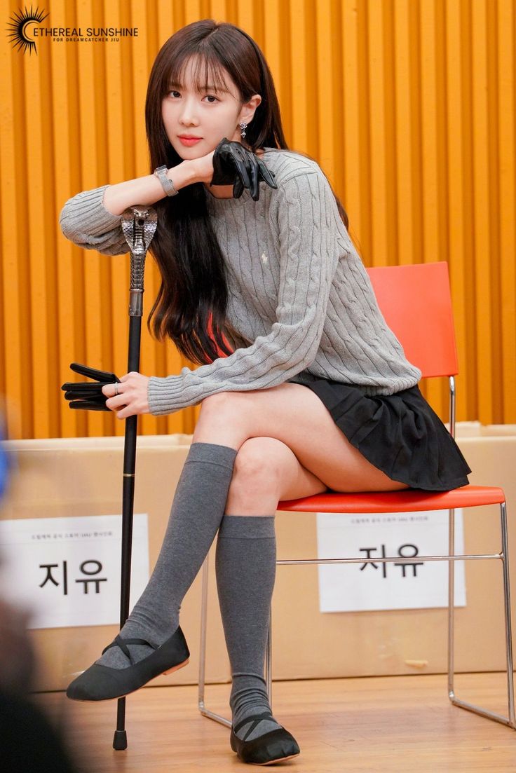 Woman with long hair in a gray sweater and black skirt sitting with a cobra cane