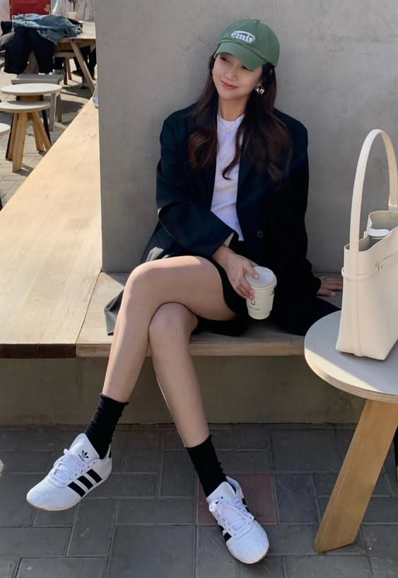 Woman in a green cap and black blazer sitting outdoors with a coffee cup