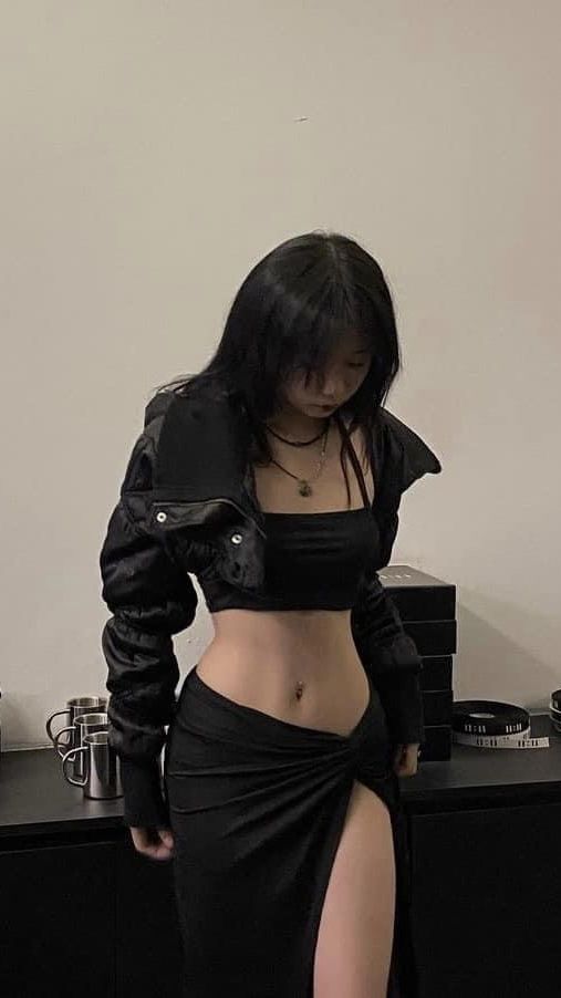 Woman with black hair wearing a black crop top and high-slit skirt indoors