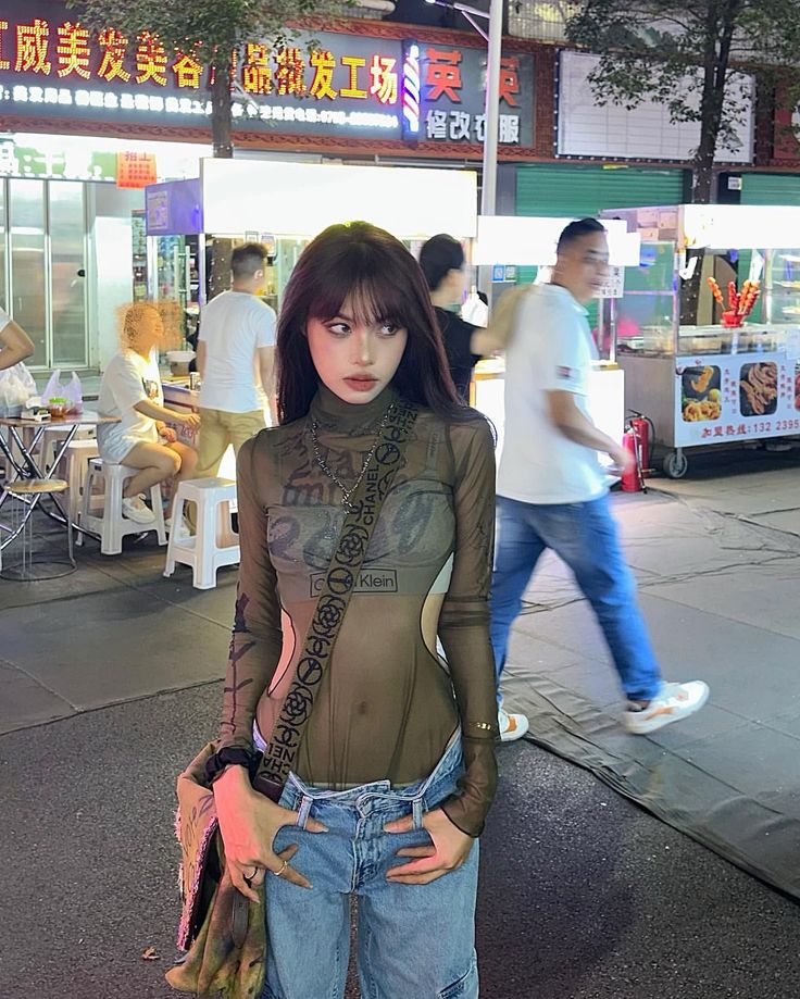 Woman in a sheer top and jeans on a busy street at night