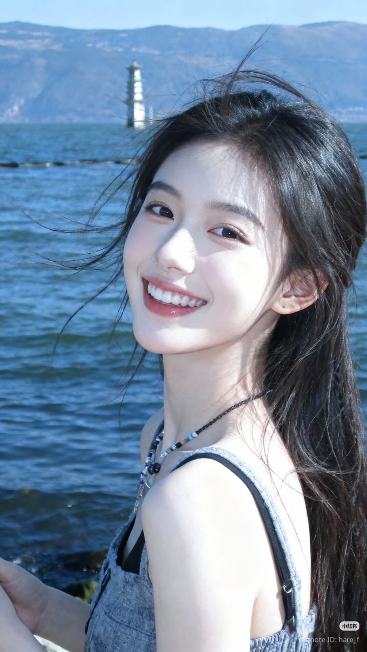 Smiling woman with long black hair by a lake with a lighthouse in the background