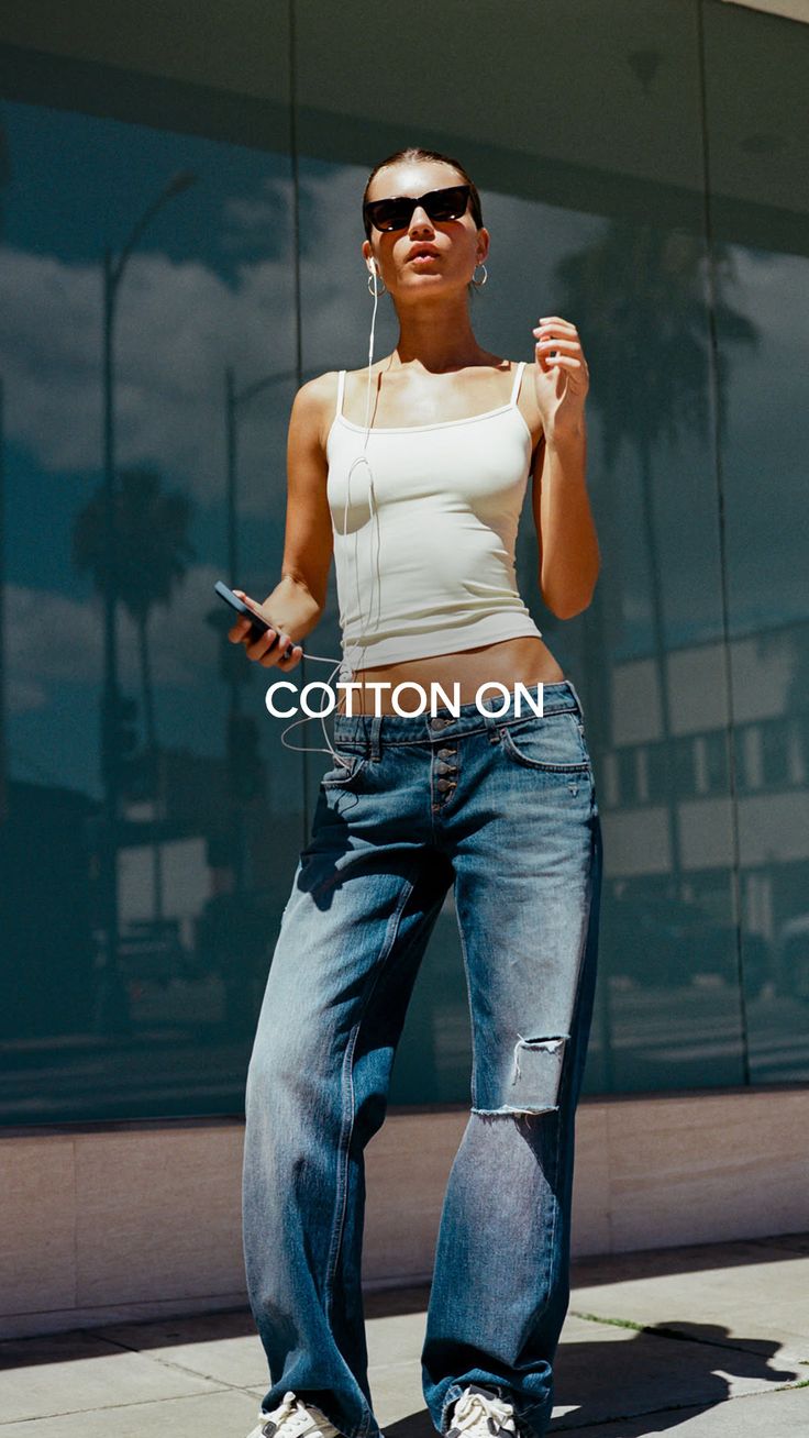 Woman in a white tank top and ripped jeans with sunglasses and earbuds outdoors