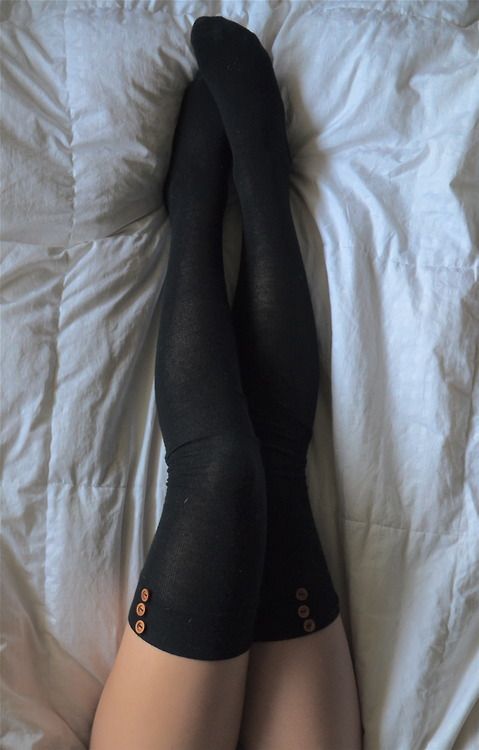 Legs in black thigh-high socks with buttons on a white bed