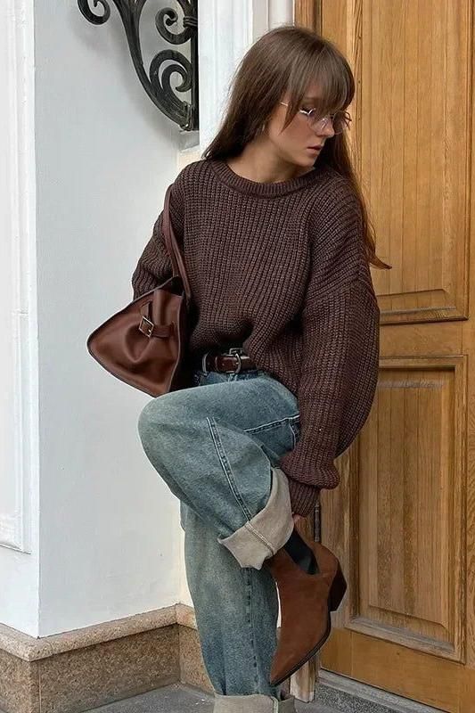 Woman in a brown sweater and blue jeans with a brown bag and boots