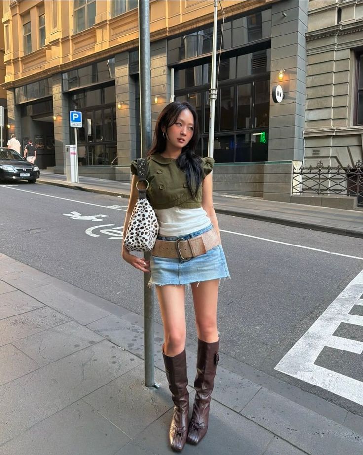 Woman in a denim skirt and knee-high boots standing on a city street