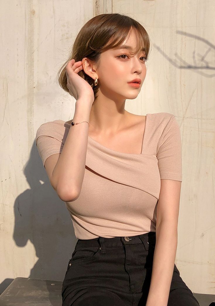 Woman with short hair wearing a beige top and black pants in soft lighting
