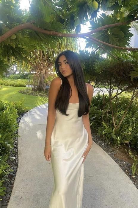 Woman in a white slip dress standing on a path in a lush garden