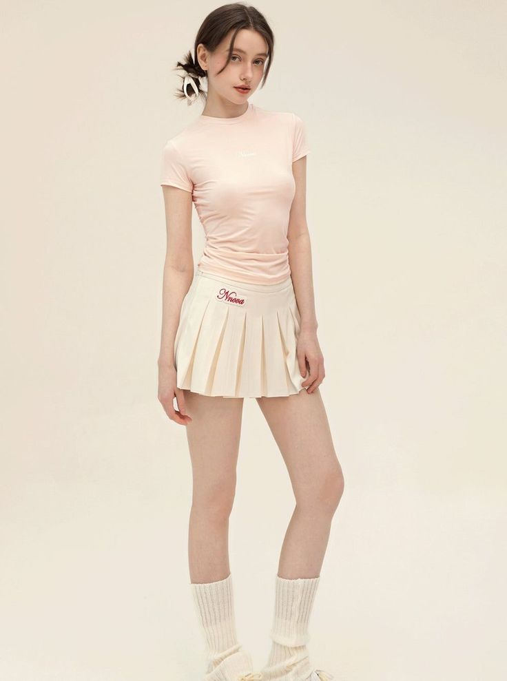 Woman in a pink top and pleated skirt with leg warmers in a studio